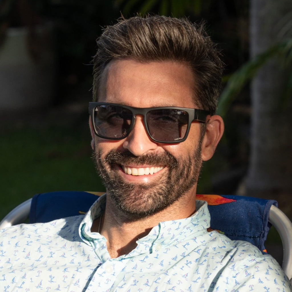 Man smiling and wearing Valley Rays The Phoenix sunglasses with matte black frames and gold mirror lenses. High-quality, eco-friendly eyewear for outdoor activities.